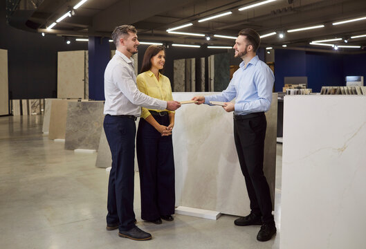 Consultant offers consultation to family couple in hardware shop, advising on materials for home renovation before purchase, providing help in a retail space focused on practical solutions.