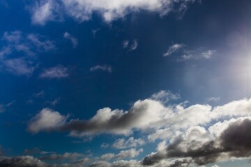 Cloud formations are drifting across deep blue sky in flat design with sunlight glare