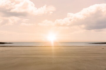 Bright sun disk is casting golden glow over sand, sea under cloud-speckled sky in flat design