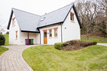 Detached cream-colored house is standing in flat design, featuring brick driveway and wheelie bins