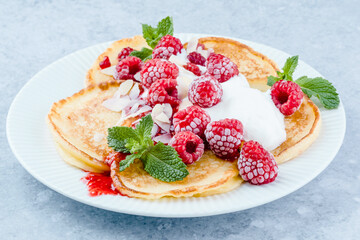 A plate of fluffy pancakes generously topped with fresh raspberries, whipped cream, and sprinkled with almond flakes, mint leaves on a gray background. Breakfast or sweet dessert concept. side view