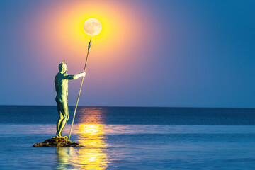 Statue of Neptune Holding Trident with Full Moon Twilight over sea horizon in the Background, beach...
