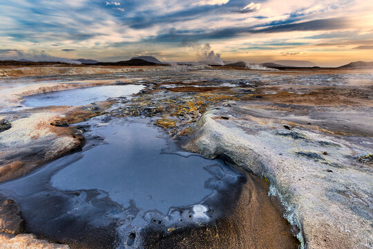 View of steaming vents and bubbling mud pools paint a surreal landscape under a dramatic sky, contrasting textures and colors in Iceland, Iceland.