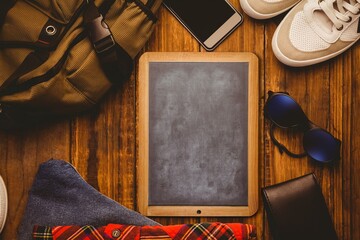 Chalkboard tablet is being shown in flat lay on wooden surface with backpack, phone and sneakers