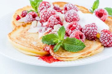 A plate of fluffy pancakes generously topped with fresh raspberries, whipped cream, and sprinkled with almond flakes, mint leaves on a gray background. Breakfast or sweet dessert concept. side view