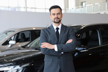 Portrait of salesman with crossed arms near new car in salon