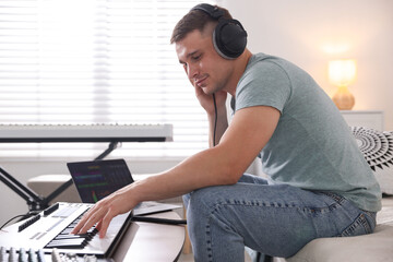 Man in headphones working with MIDI keyboard at table indoors