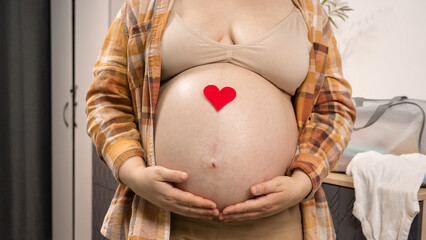 Pregnant woman holding red heart shape and feel love for unborn baby in belly. Awaiting for baby. Concept of maternity and pregnancy care