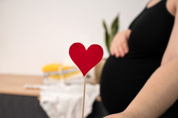 Pregnant woman holding red heart shape and feel love for unborn baby in belly. Awaiting for baby. Concept of maternity and pregnancy care