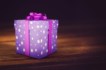 Purple polka dot gift box is sitting on wooden tabletop, showing pink ribbon and warm lighting