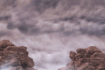 Flat design showing two red-brown sandstone formations rising under gray storm clouds