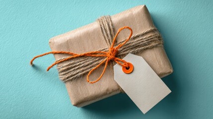 A small, neatly wrapped gift box tied with natural twine and an orange string bow, featuring a blank white tag on a textured blue background.