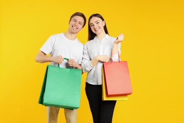 Happy couple with shopping bags on yellow background