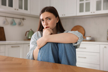 Worried woman suffering from paranoia at table in kitchen