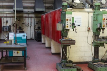 Two green drill presses are standing in flat design workshop with red lockers, workbench, ducts