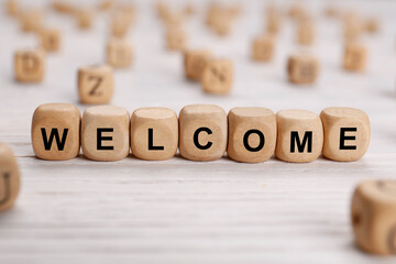 Word Welcome made of wooden cubes on white table, closeup