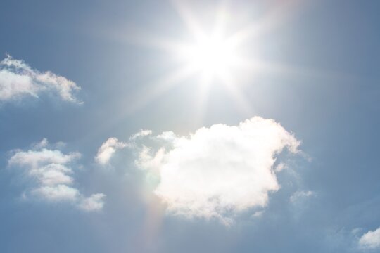 Fototapeta Sun is radiating beams and lens flare rays across flat design sky with scattered cumulus clouds