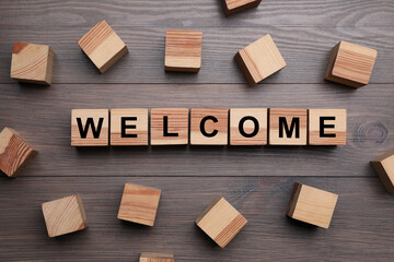 Word Welcome made of wooden cubes on table, flat lay
