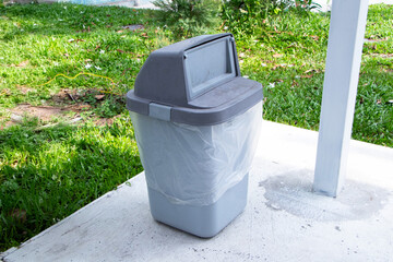 Rubbish bin garbage square shape grey with flip cover on green grass is background in park. Old...