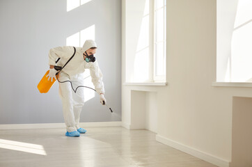 Portrait of service man wearing protective ppe suit and face mask disinfecting empty apartment or...