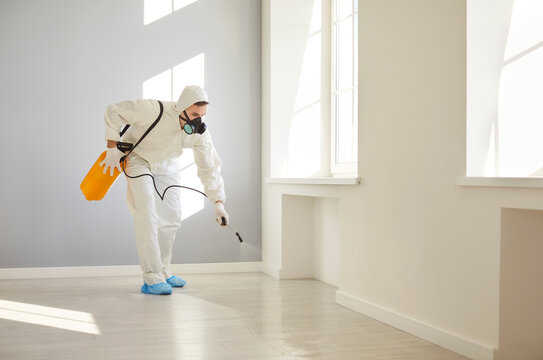 Portrait of service man wearing protective ppe suit and face mask disinfecting empty apartment or doing pest control with disinfectant spray. Home disinfection and protection concept. - Powered by Adobe