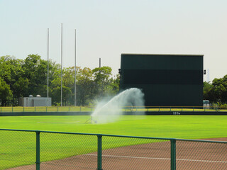 The sprinkler is watering the lawn of the baseball ground.
