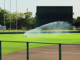 The sprinkler is watering the lawn of the baseball ground.