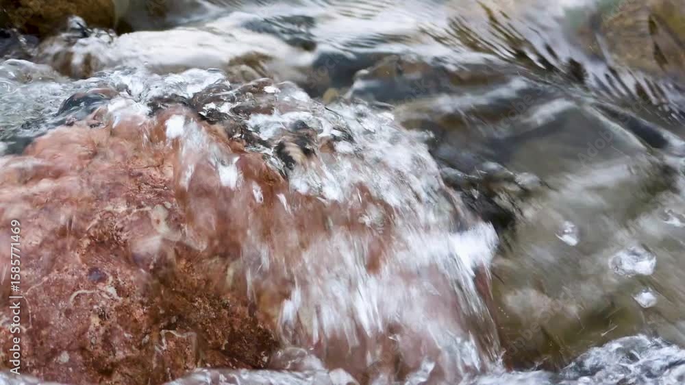 Poster a close-up view of smooth stones partially submerged in a gently flowing stream, with water cascadin
