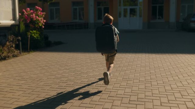Excited Schoolboy with Backpack Running Toward School on a Sunny Day