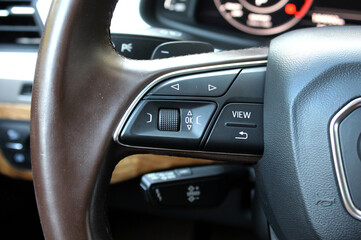Close up of premium car brown leather steering wheel with multifunctional control buttons, textured...