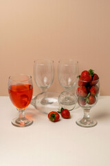 Creative still life with glassware. Aglass of strawberry drink, another filled with fresh strawberries, and empty glasses on a table.