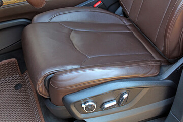 Close-up of brown leather car seat with visible stitching and electronic adjustment controls. The...
