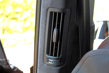 Close-up of a rear seat air vent on the B-pillar. Matte black plastic vent with vertical slats and...