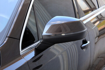 Glossy black side mirror of a modern car with integrated turn signal. Aerodynamic shape, chrome...