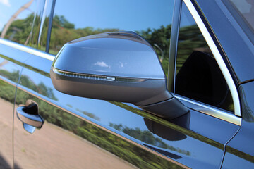 Glossy black side mirror of a modern car with integrated turn signal. Aerodynamic shape, chrome...
