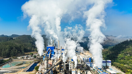 Imagem aérea mostra complexo industrial de papel e celulose com chaminés e caldeiras em funcionamento, evidenciando poluição e impacto ambiental
