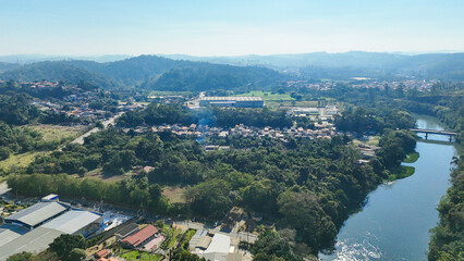 Vista aérea de uma área urbana cercada por vegetação densa, casas, ruas e pequenas construções. Cena harmoniosa entre natureza e ocupação humana, revelando equilíbrio ambiental e cotidiano local © RNL Fotografia