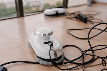 Modern robot window cleaner charging on floor by dirty large window, preparing for automatic...