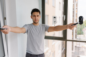 Portrait of young man controlling cleaning robots on skyscraper window using remote control,...