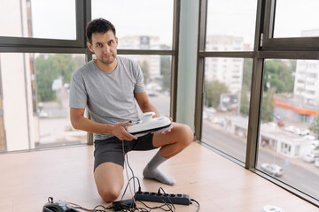 Portrait of window cleaner male kneeling on floor and preparing window cleaning robot in modern...