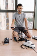 Vertical portrait of confused man crouching among tangled window cleaning robot cables,...