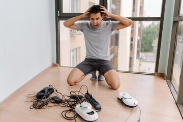 Stressed screaming window cleaner male kneeling on balcony, gripping head amid broken robots,...