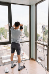 Rear view of housekeeper male using advanced robotic device for cleaning large window in modern...