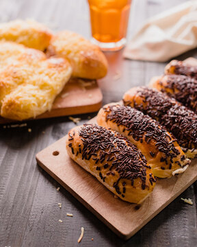 Assorted Indonesian sweet breads served on wooden cutting boards, including chocolate sprinkles bread (roti coklat meses) and cheese-topped bread (roti keju), perfect for food blogs, menu designs.