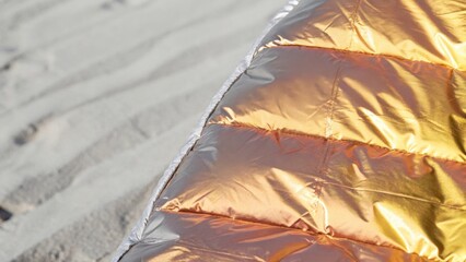 Metallic emergency blanket gleaming on pale sand, radiating solar light while offering critical survival protection