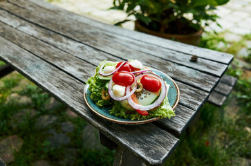 Plate of salad with lettuce, tomatoes, and onions sits on a wooden table