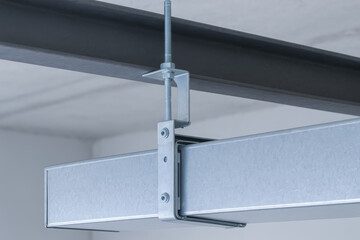 Metal air duct suspended from ceiling beam with engineering support bracket in industrial building environment