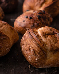 Close-up of freshly baked artisanal bread rolls topped with mixed seeds and grains. Rustic golden crust with a textured surface, displayed on a dark wooden background, perfect for bakery and food phot