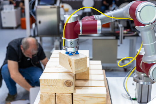 Collaborative industrial robot arm operating alongside blurred human worker while stacking wooden blocks in a smart factory environment