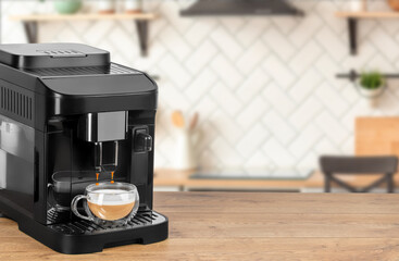 A compact black coffee machine pours a fresh cappuccino into a clear glass cup on a wooden surface...